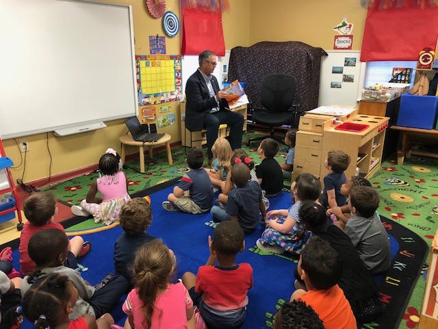 Person reading a book to a group of children in a classroom