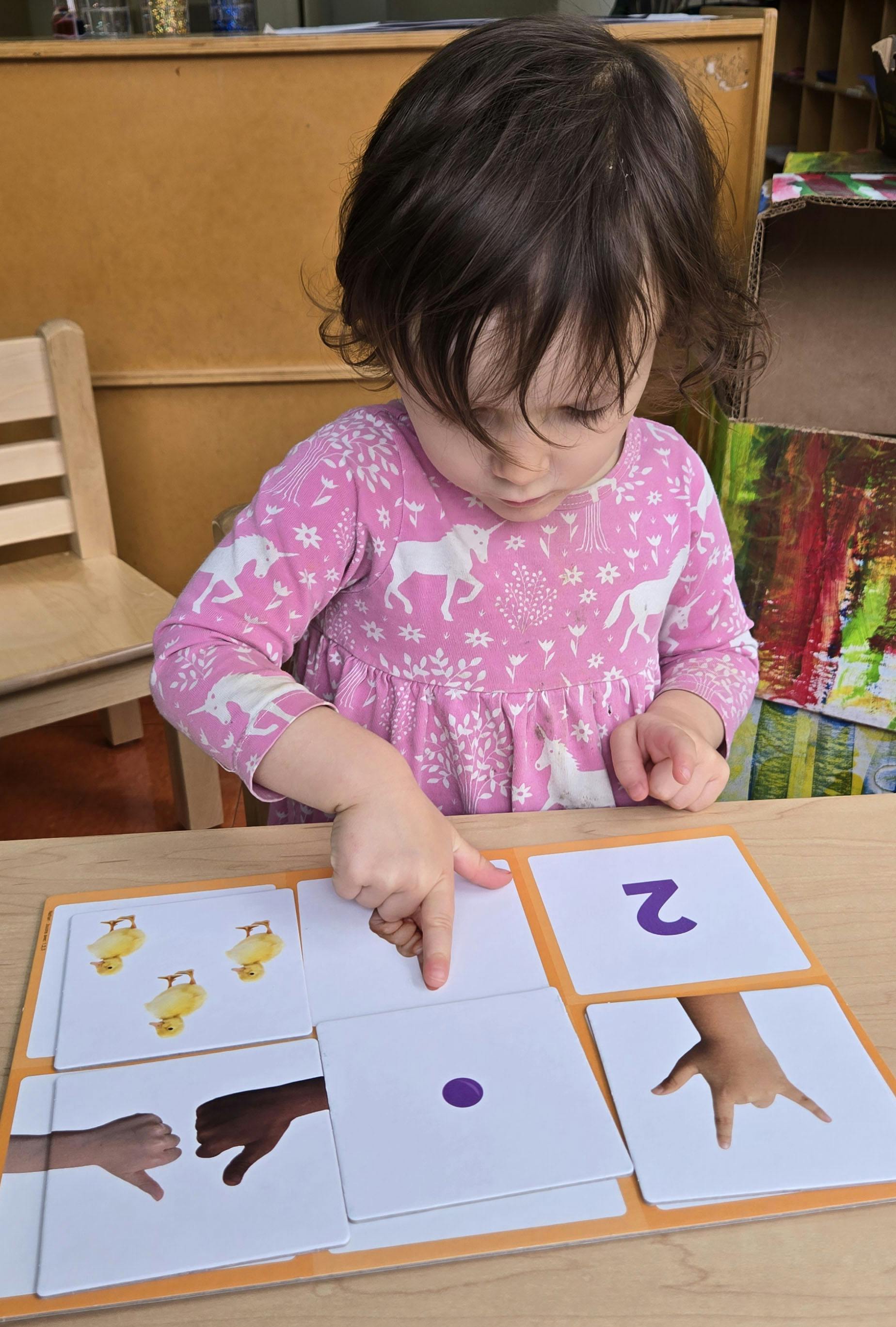 Child pointing at a learning board with cards showing numbers and hands