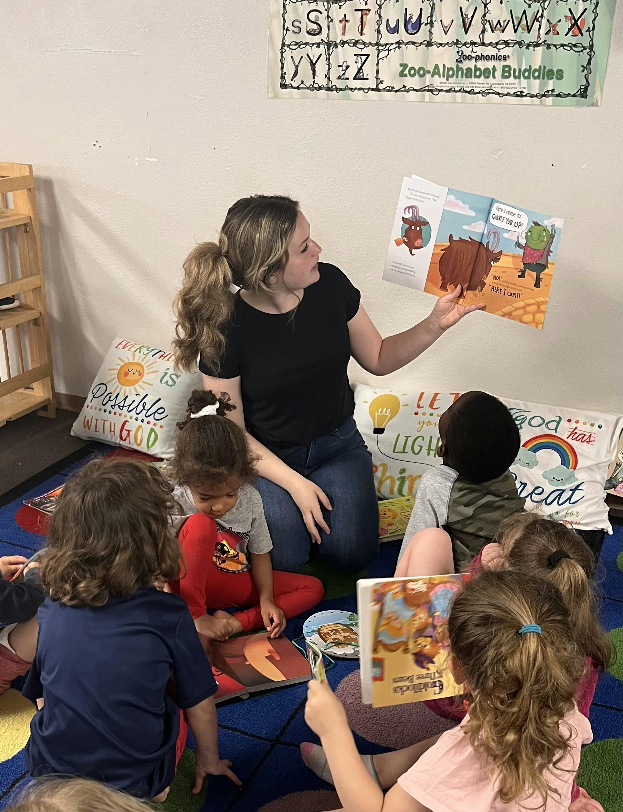 Adult reading a book to a group of children sitting on the floor