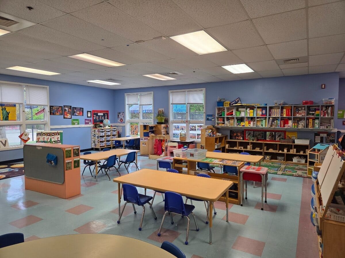 Classroom with small tables, chairs, and shelves filled with books and supplies