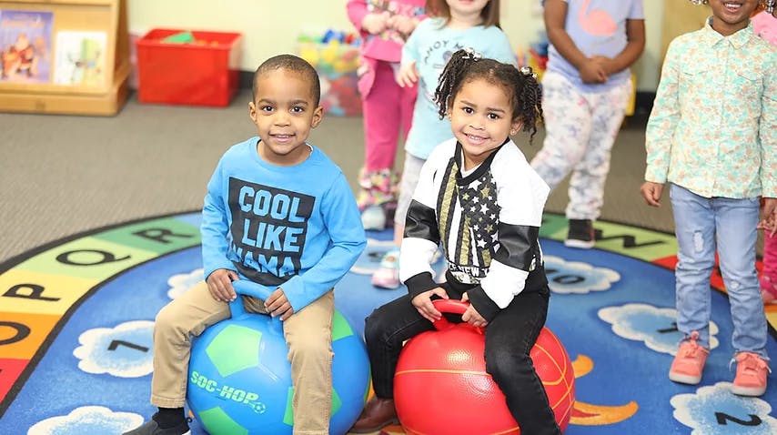 Two children sitting on bouncy balls in a classroom