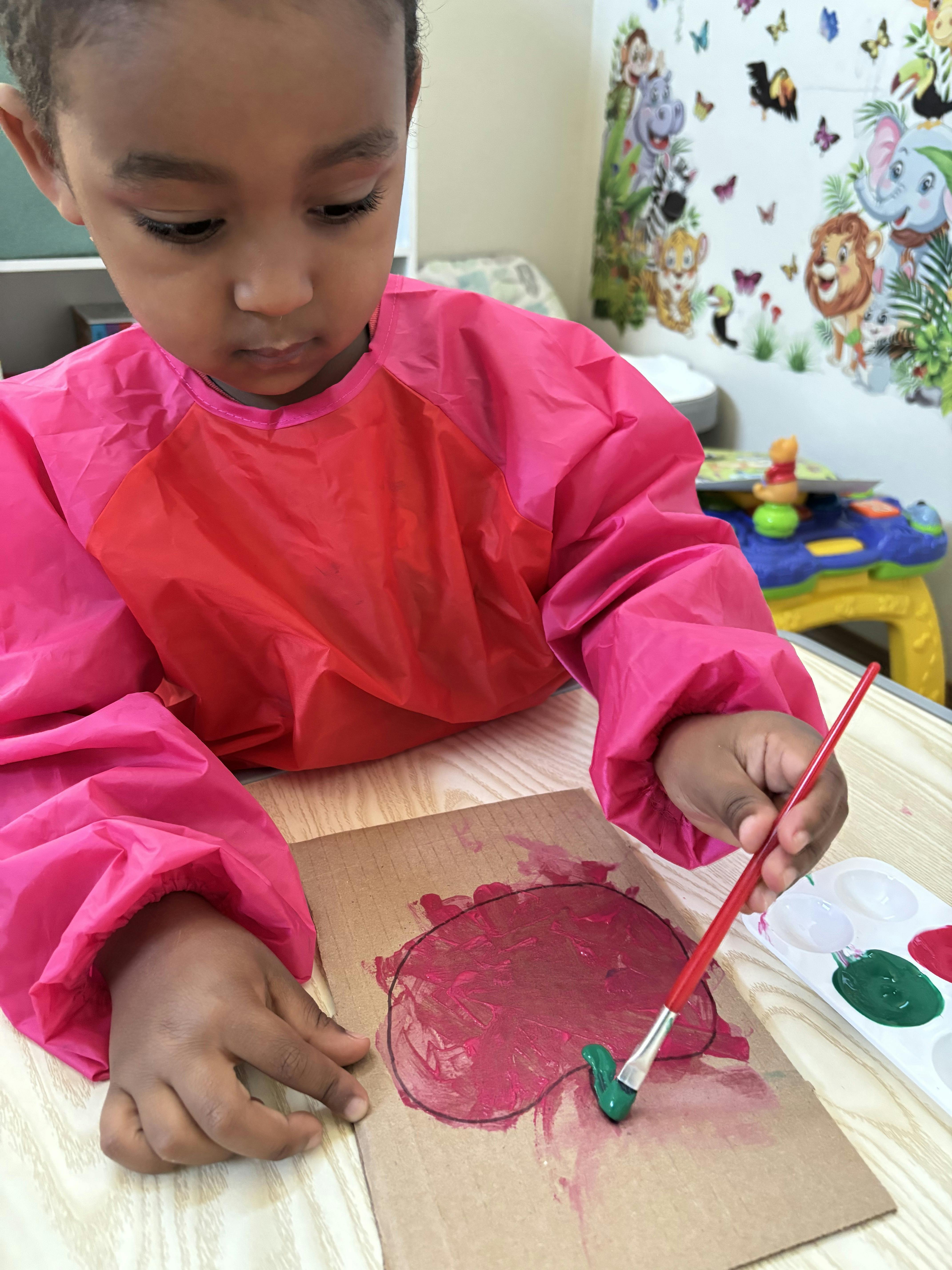Child wearing an art smock and painting on cardboard with a paintbrush