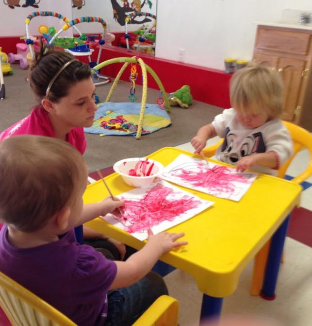 Person watching two children painting at a yellow table