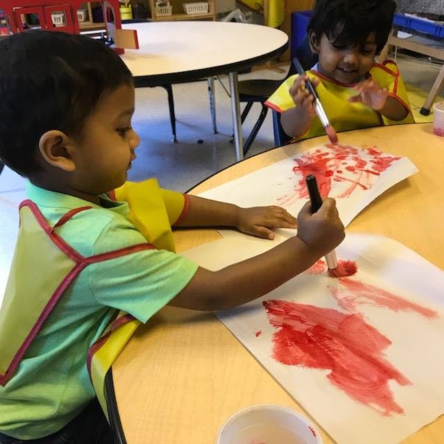 Two children painting with red paint in a classroom