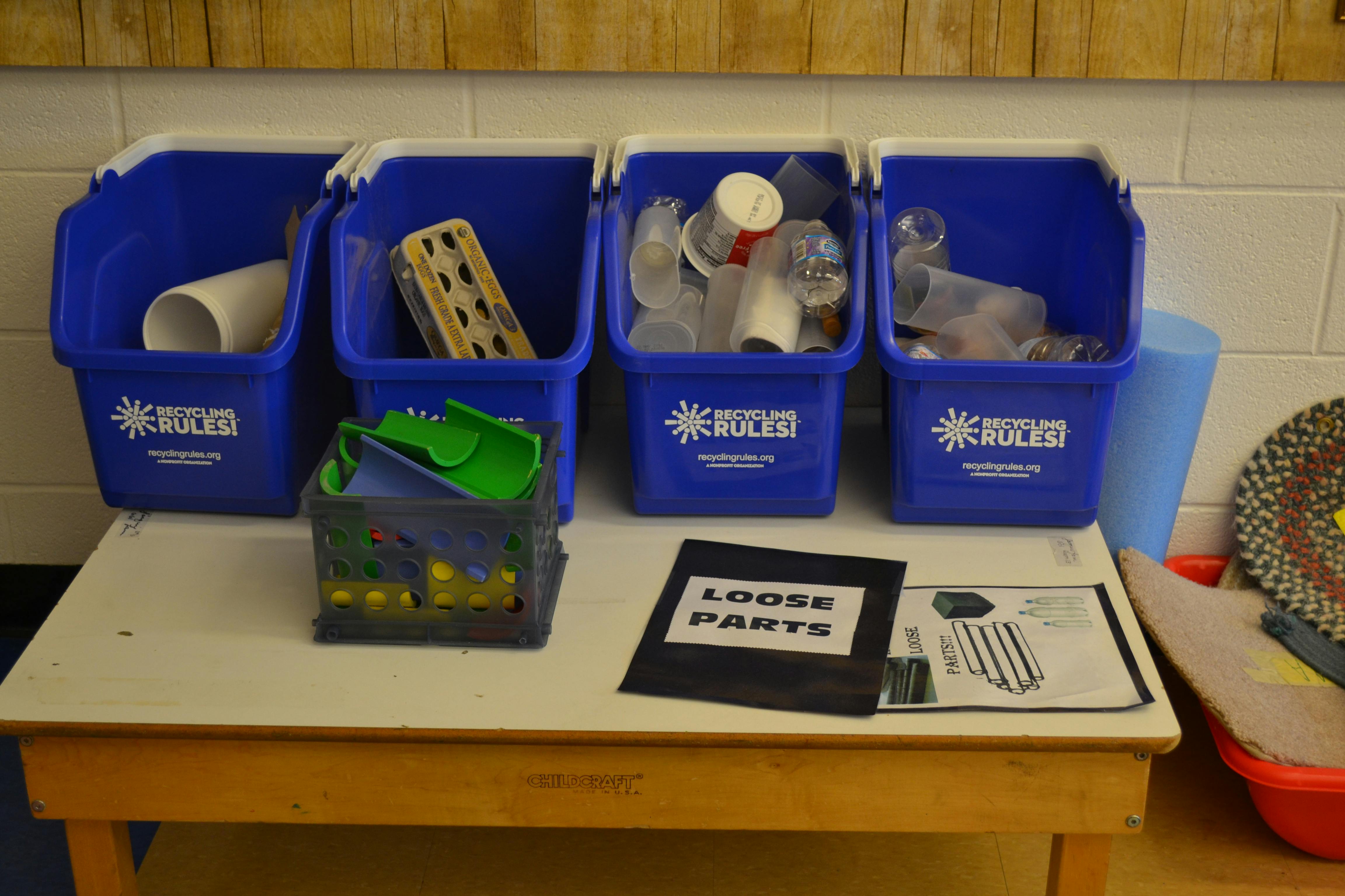 Four blue bins with various items on a table, one bin with "Loose Parts" sign
