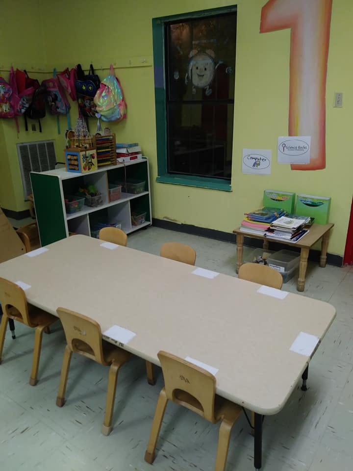 Classroom with a long table and chairs, shelves, and backpacks hanging backpacks