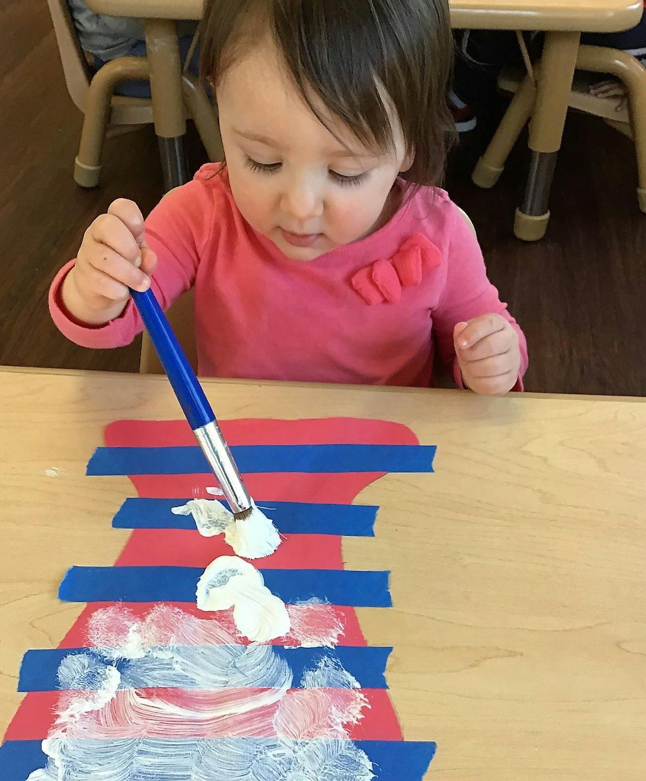 Child painting on paper with blue tape on a table