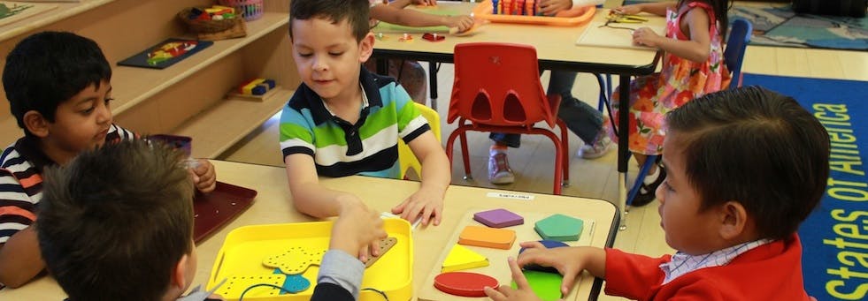 Children playing with colorful shapes at a table in a classroom