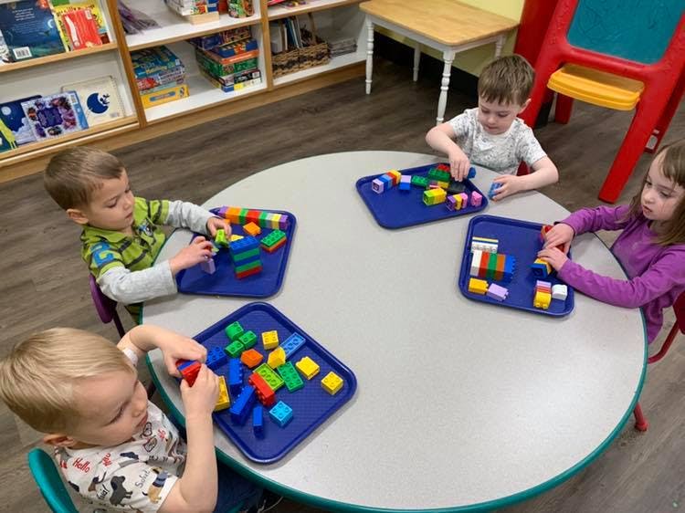 Four children playing with colorful building blocks at a round table