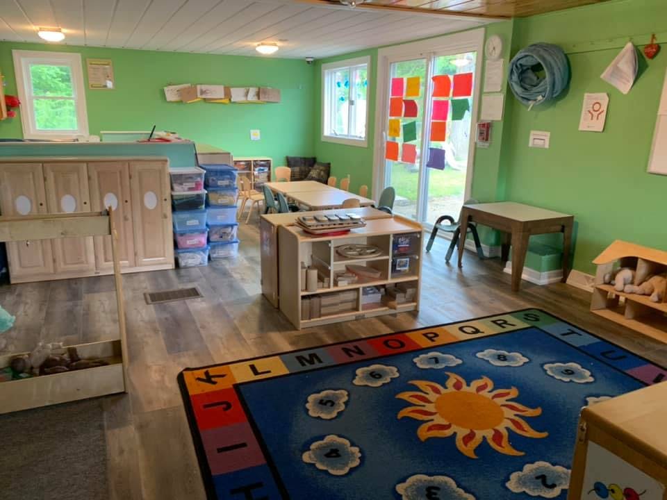 Classroom with green walls, tables, storage, and a sun rug