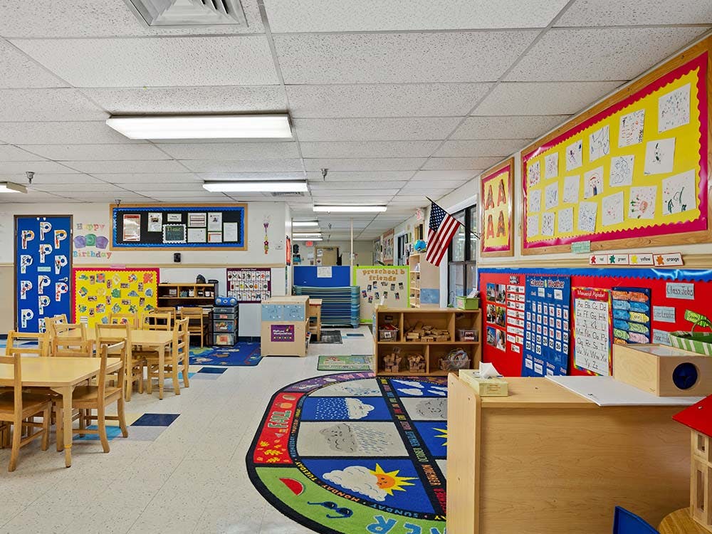 Classroom with small wooden tables and chairs, and colorful rugs and wall decorations