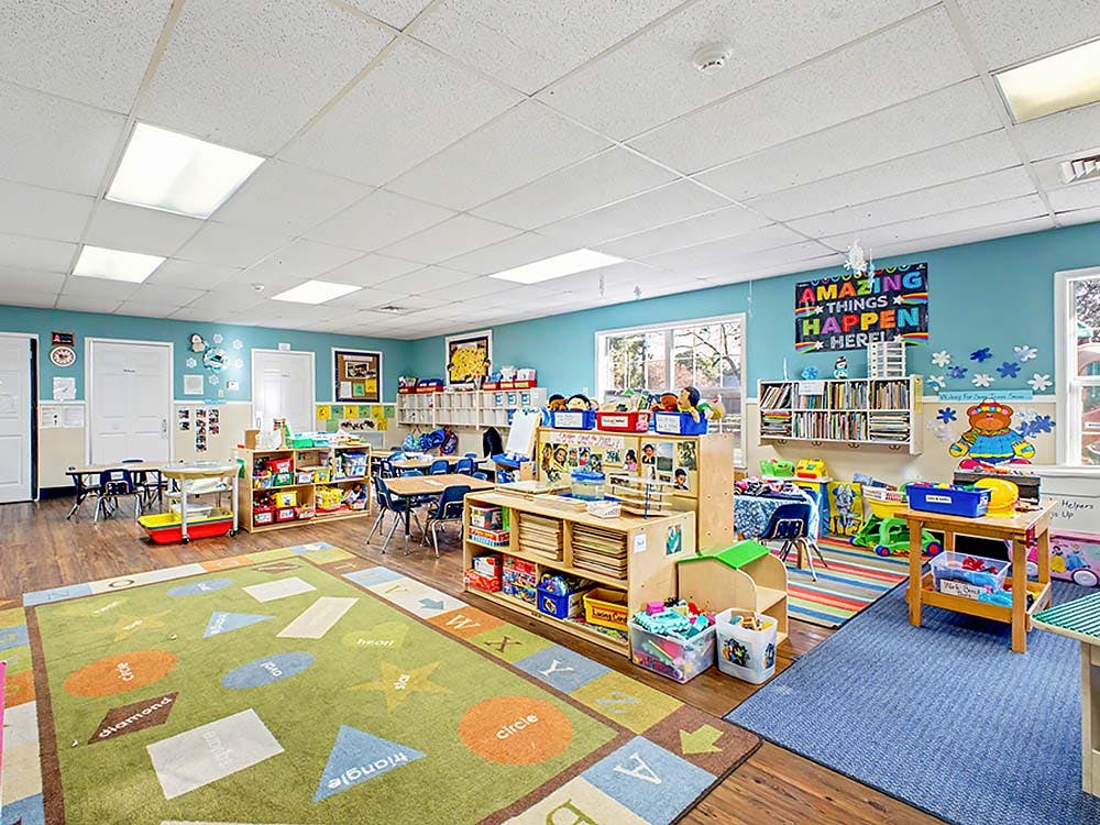 Colorful empty classroom with tables, chairs, shelves, and a rug with shapes and letters