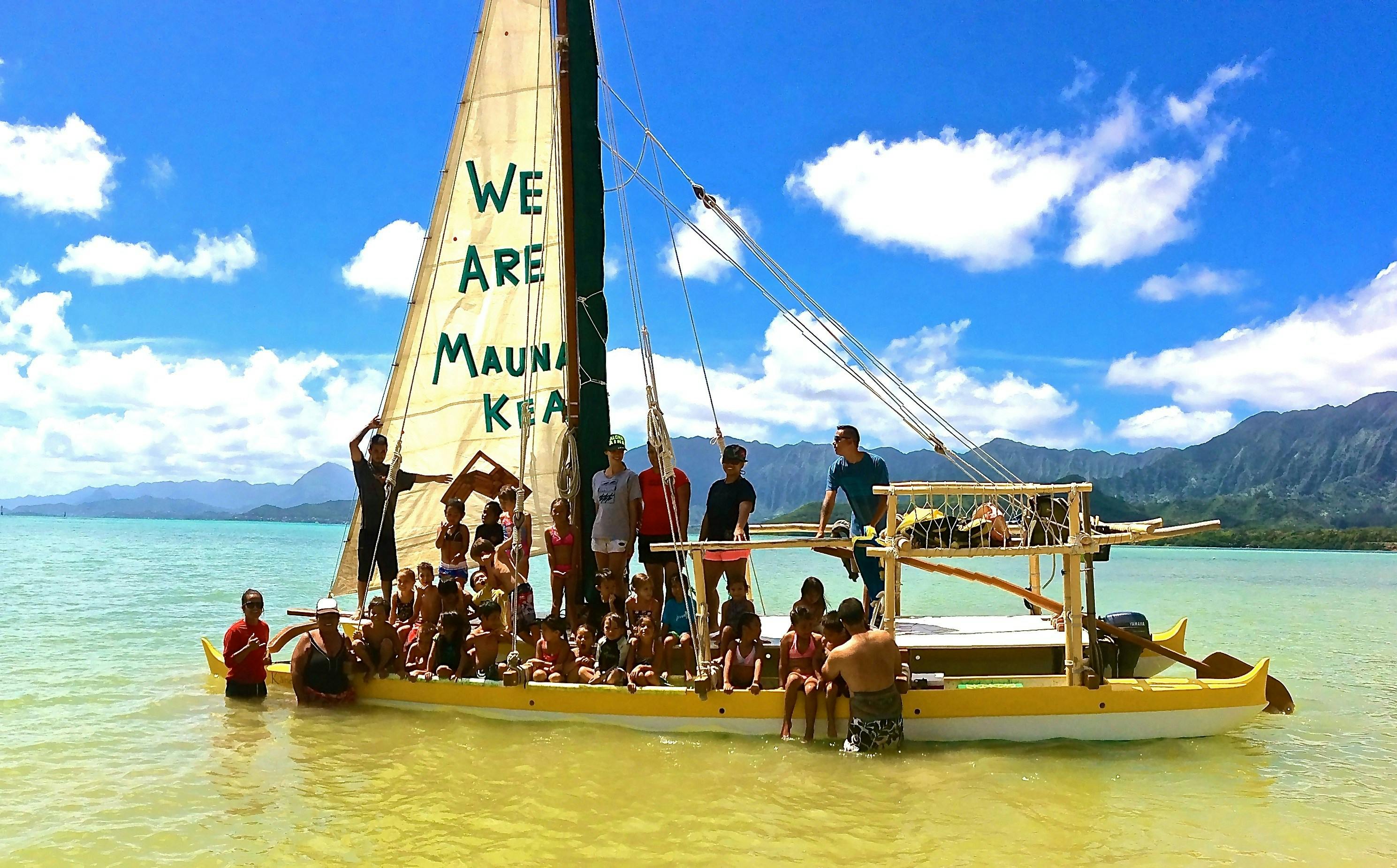 People on a sailboat with "WE ARE MAUNA KEA" on the sail