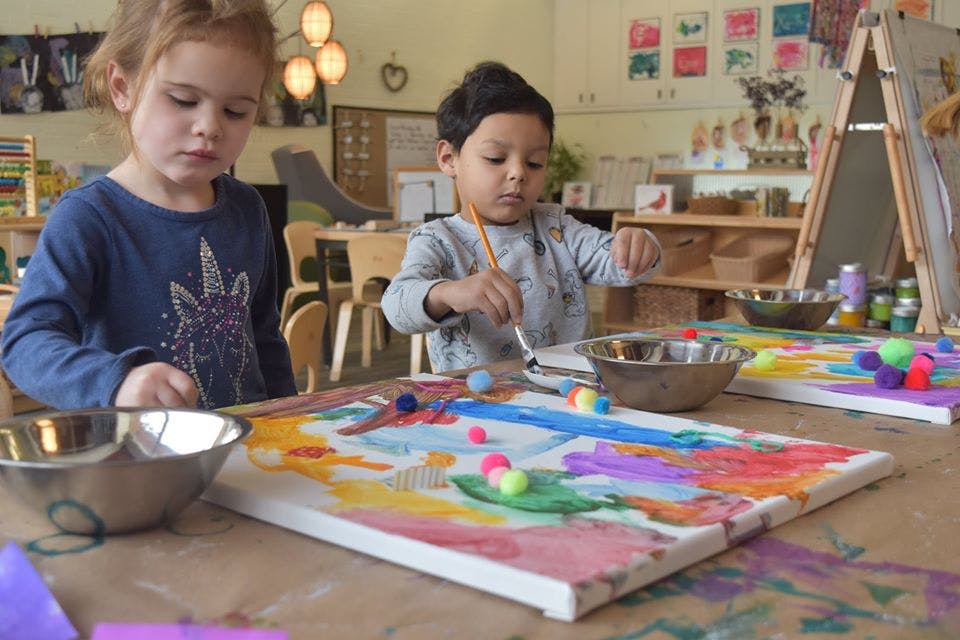 Two children painting and decorating canvases in a classroom
