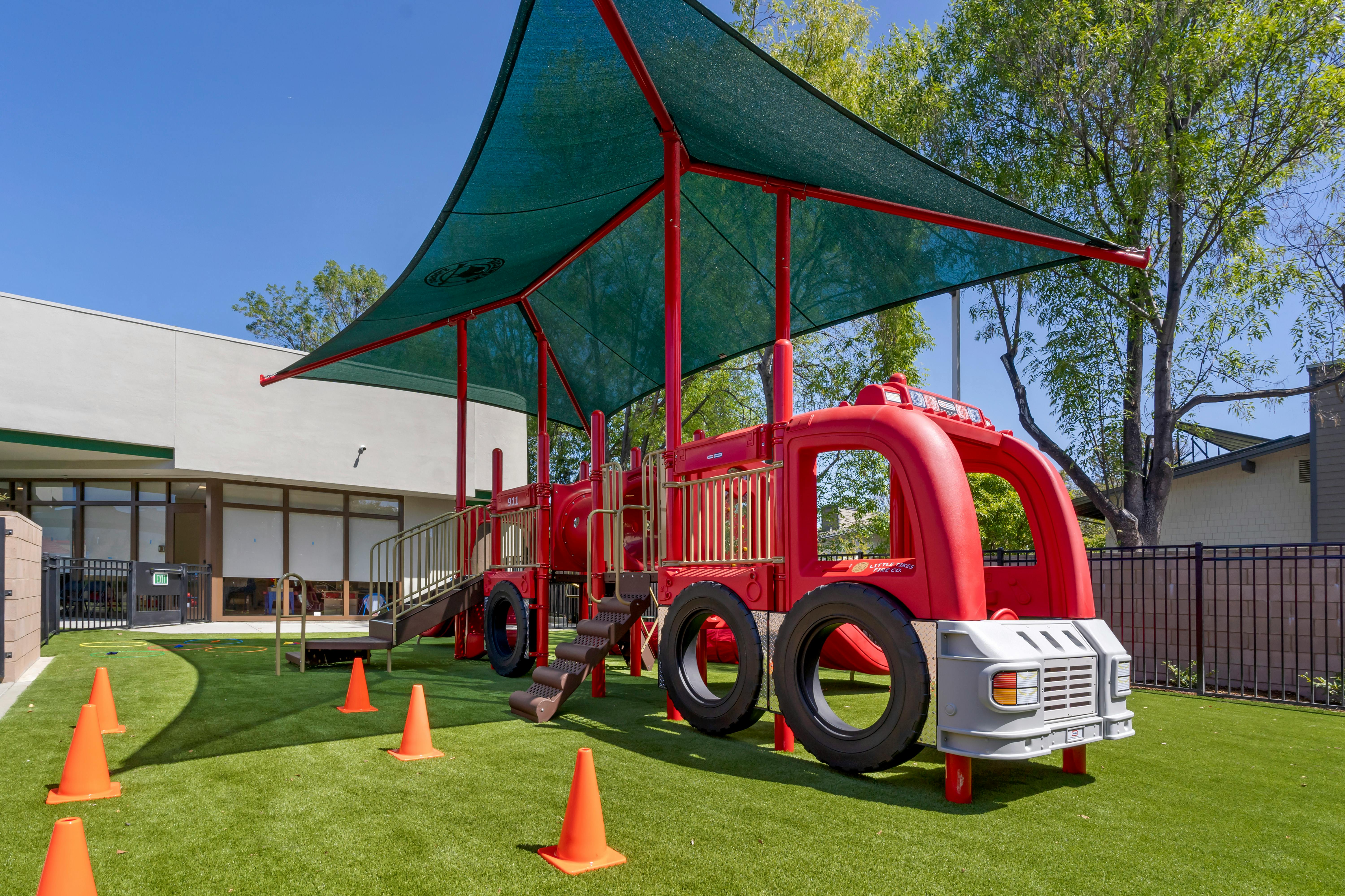 Red fire truck playground structure on green turf with shade covering