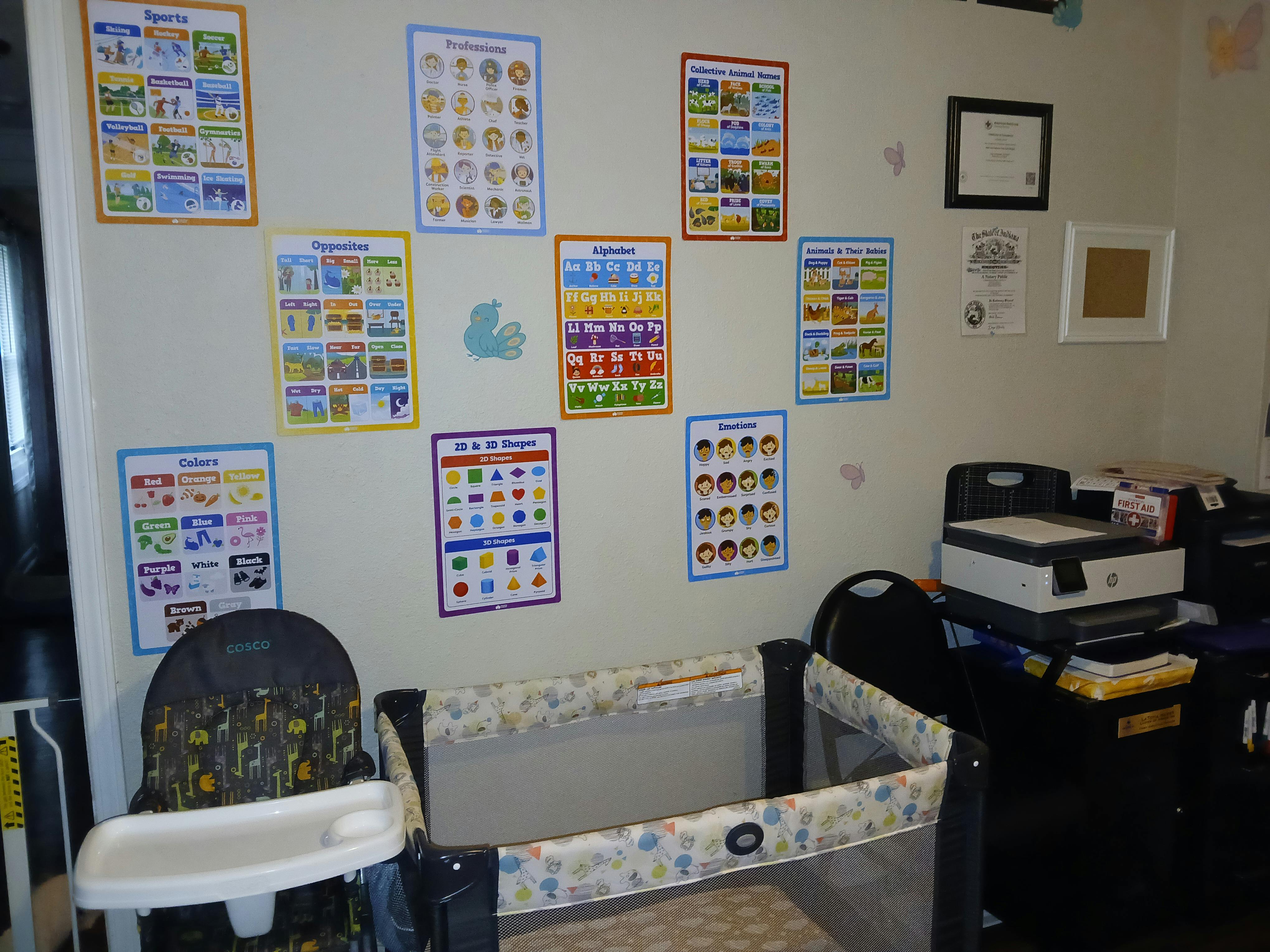 Wall with educational posters, a high chair, and a playpen