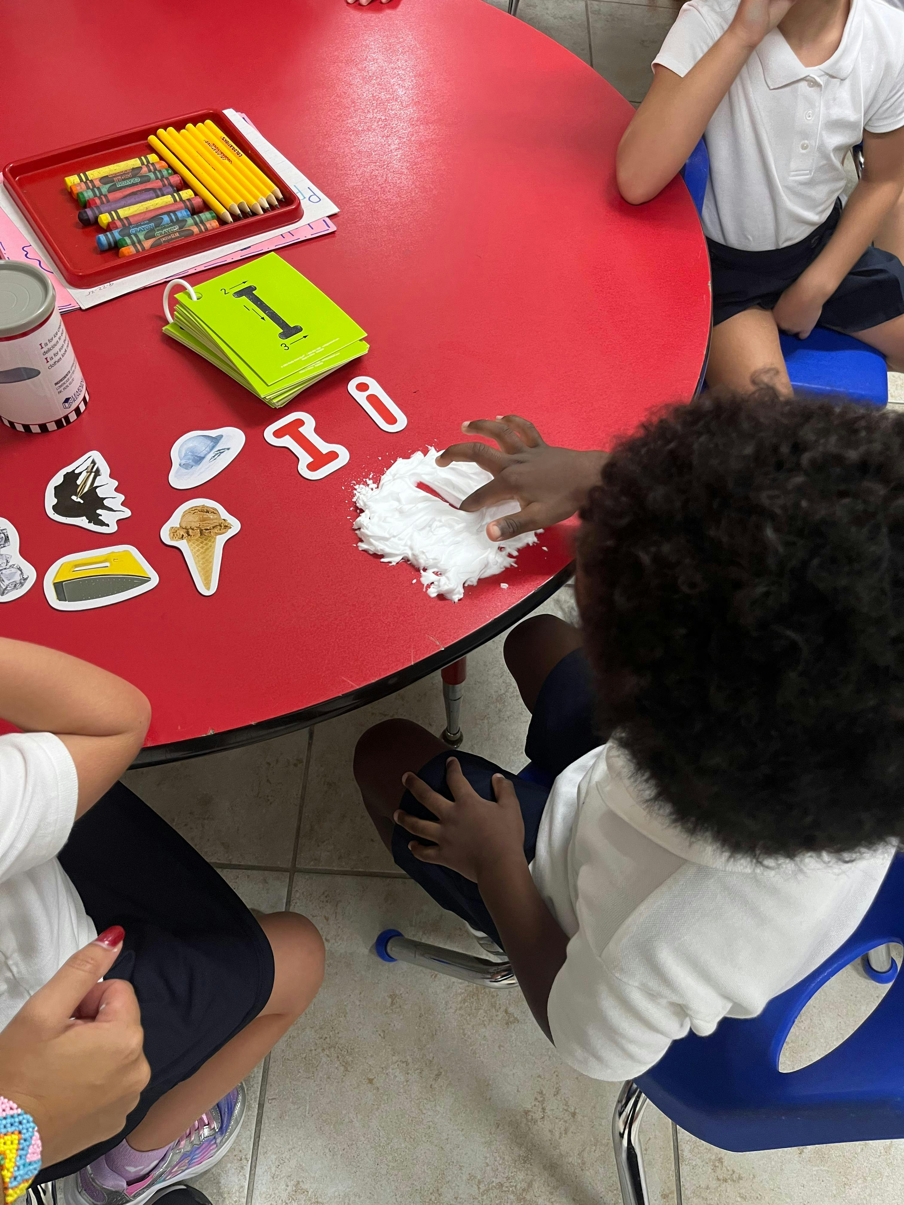 Child's hand touching white fluffy material on a red table with craft supplies