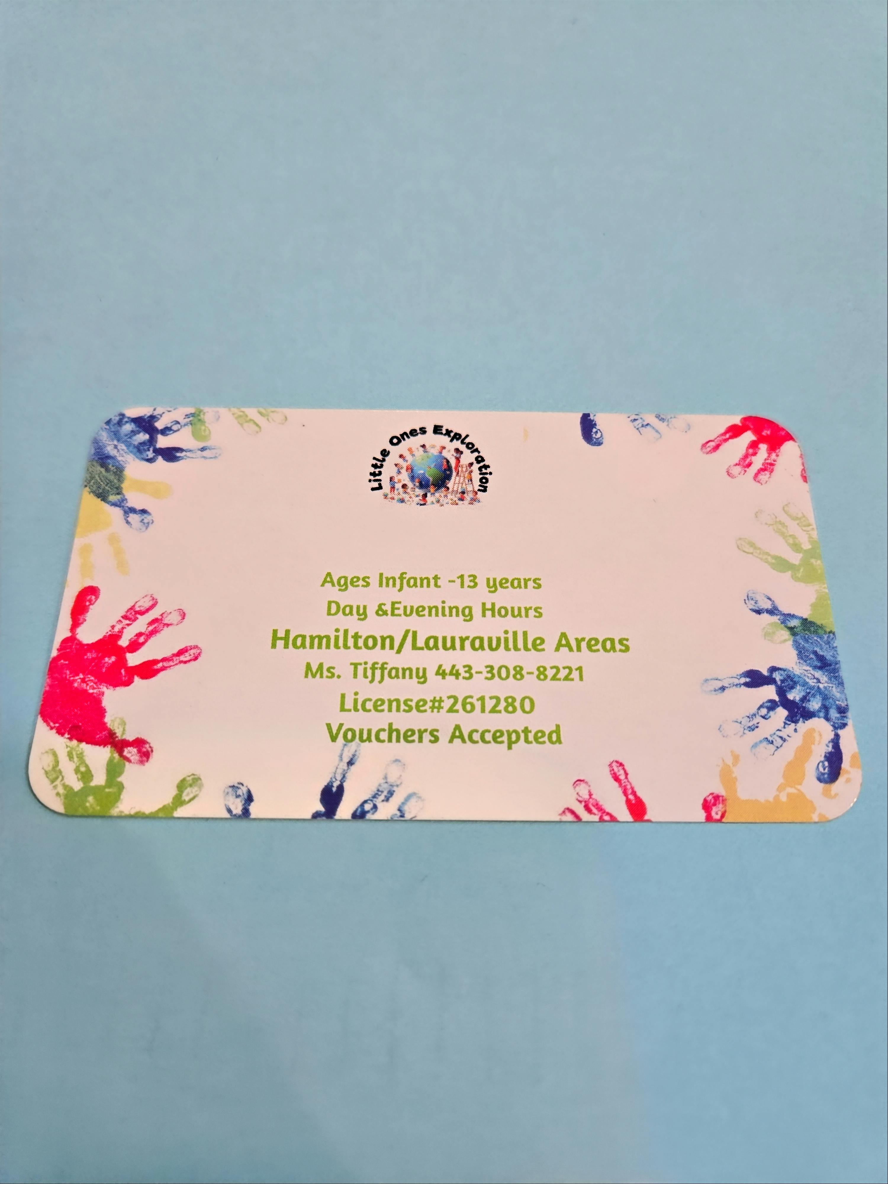 A business card with colorful handprints around the edges and text for "Little Ones Exploration"