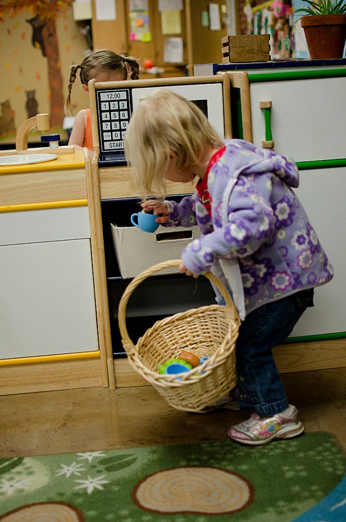 Child holding a basket and a small cup in a play kitchen