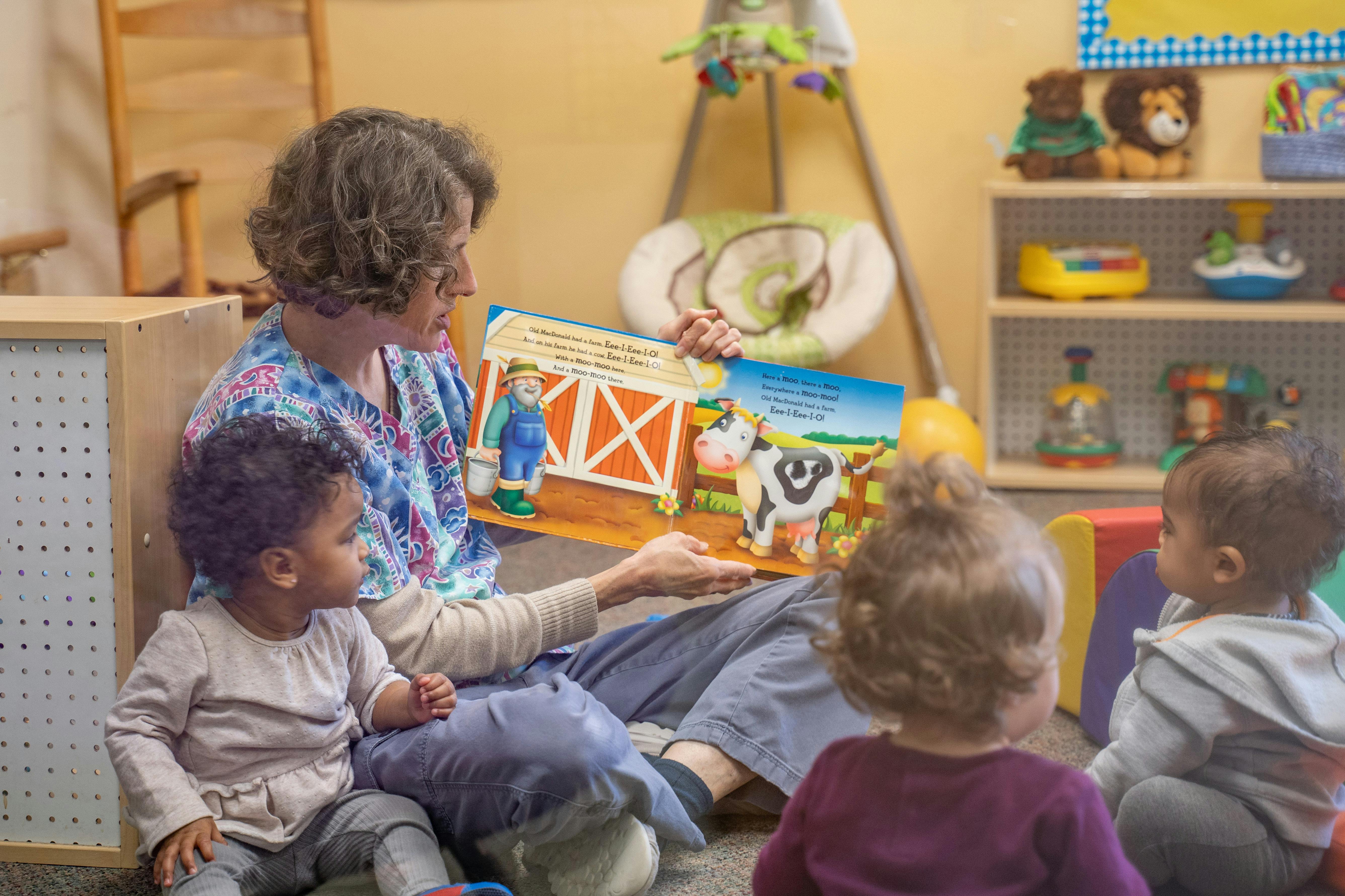 Person reading a picture book to three children in a classroom