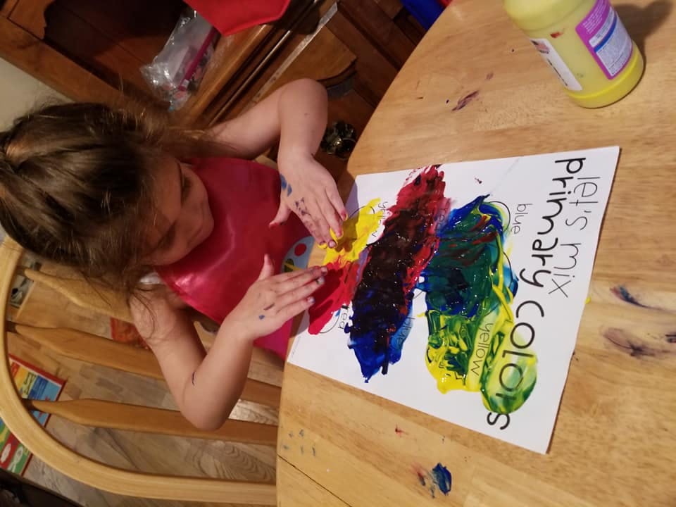 Child finger painting on a paper that says "Let's mix primary colors"