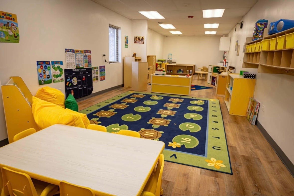Childcare classroom with colorful rug, small tables, and learning materials on walls