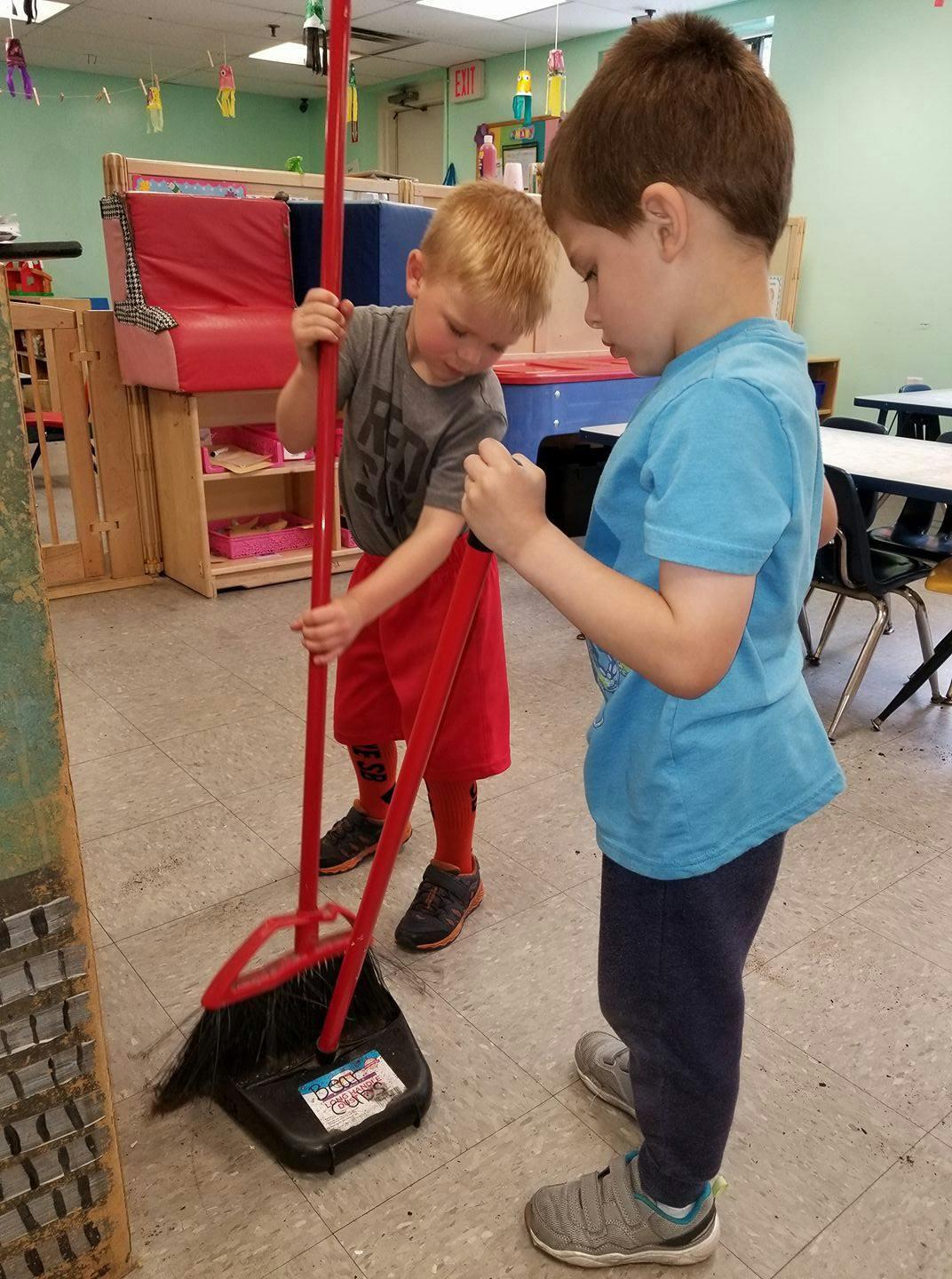 Two children sweeping with a broom and dustpan in a classroom
