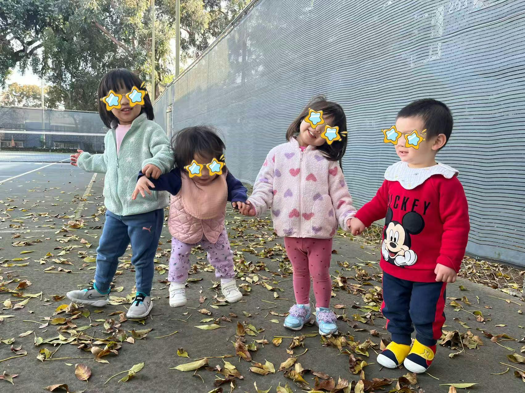 Four children holding hands on a path covered with leaves