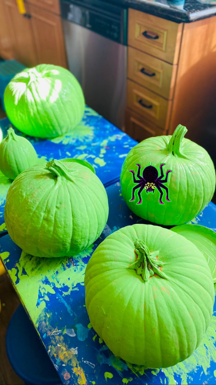 Green painted pumpkins, one with a spider sticker, on a blue and green surface