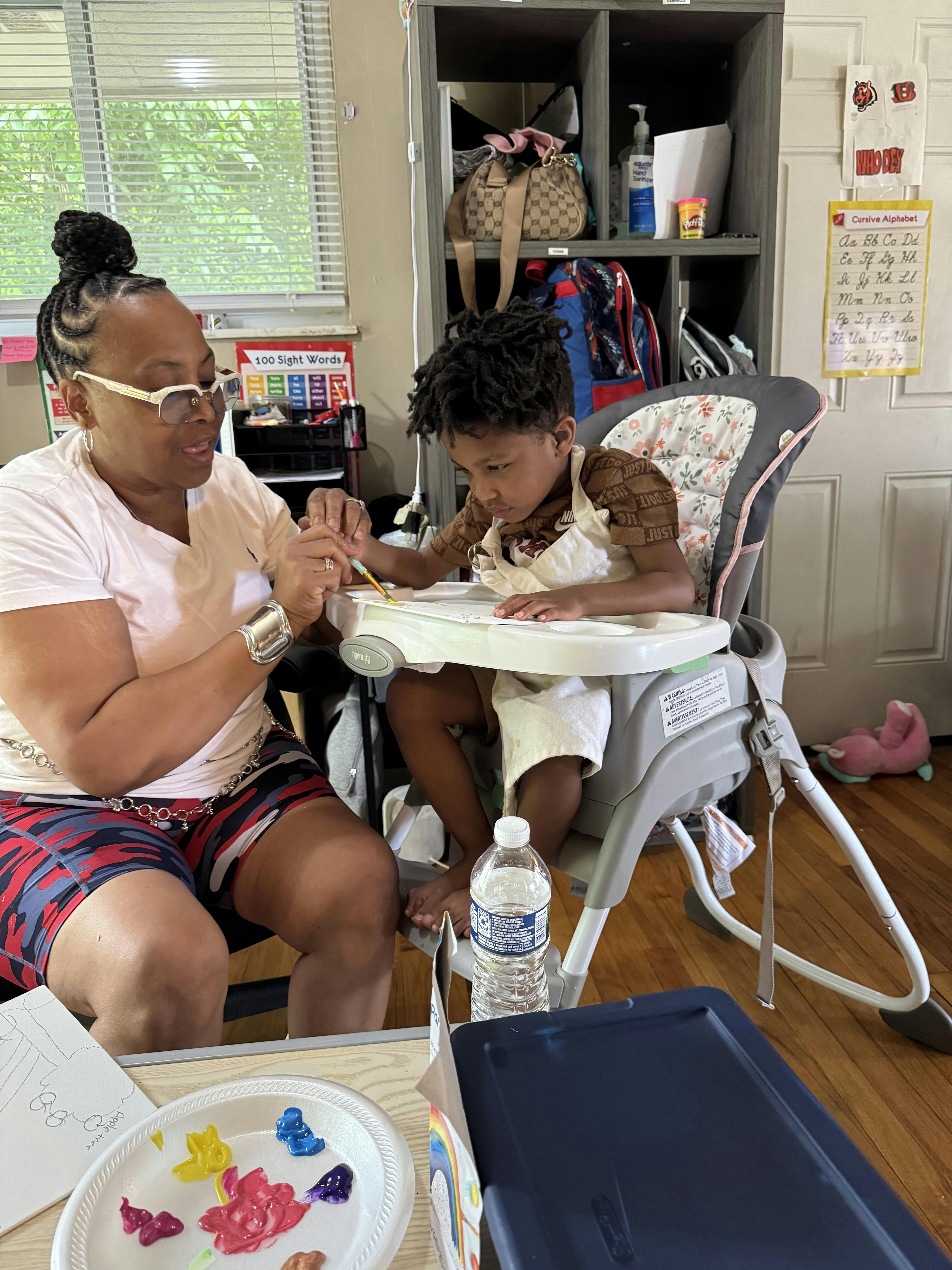 Adult helping a child paint a picture at a table
