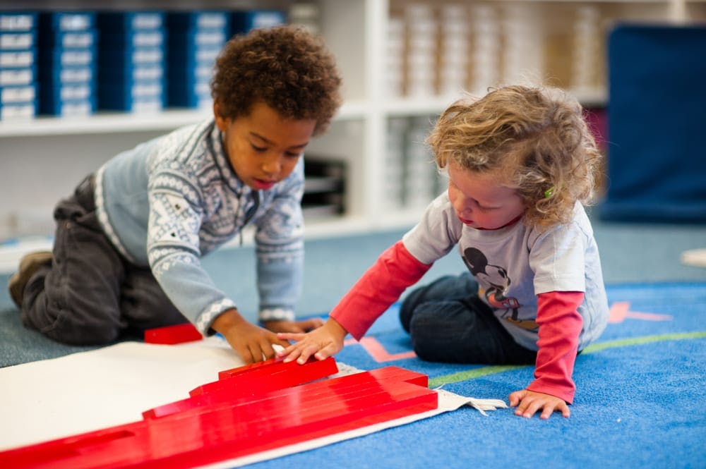 Two children playing with red blocks on the floor