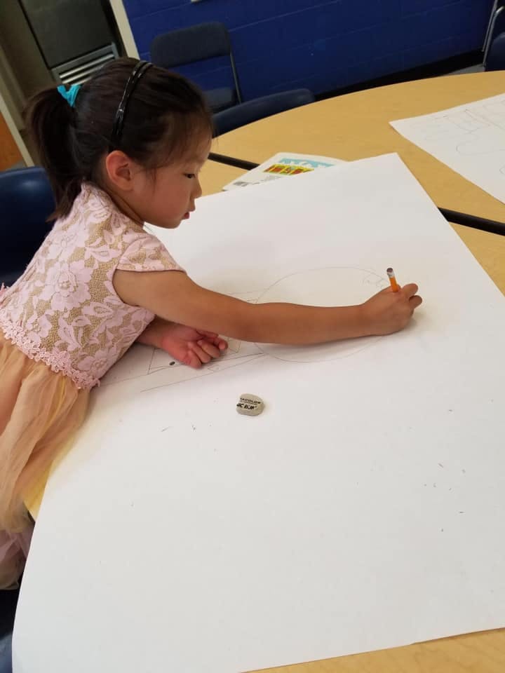 Child drawing on a large sheet of paper with a pencil