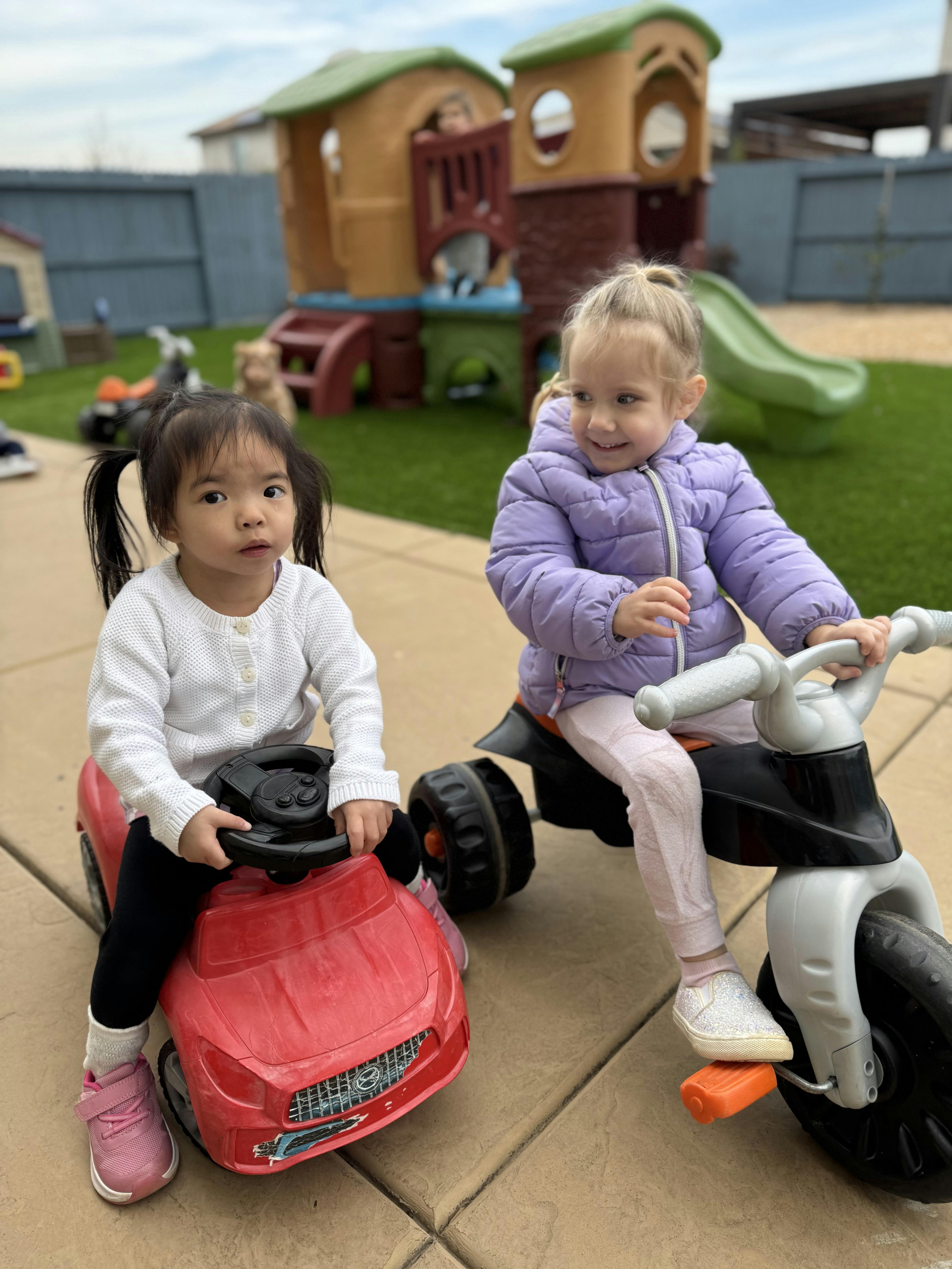 Two children playing on ride-on toys outdoors