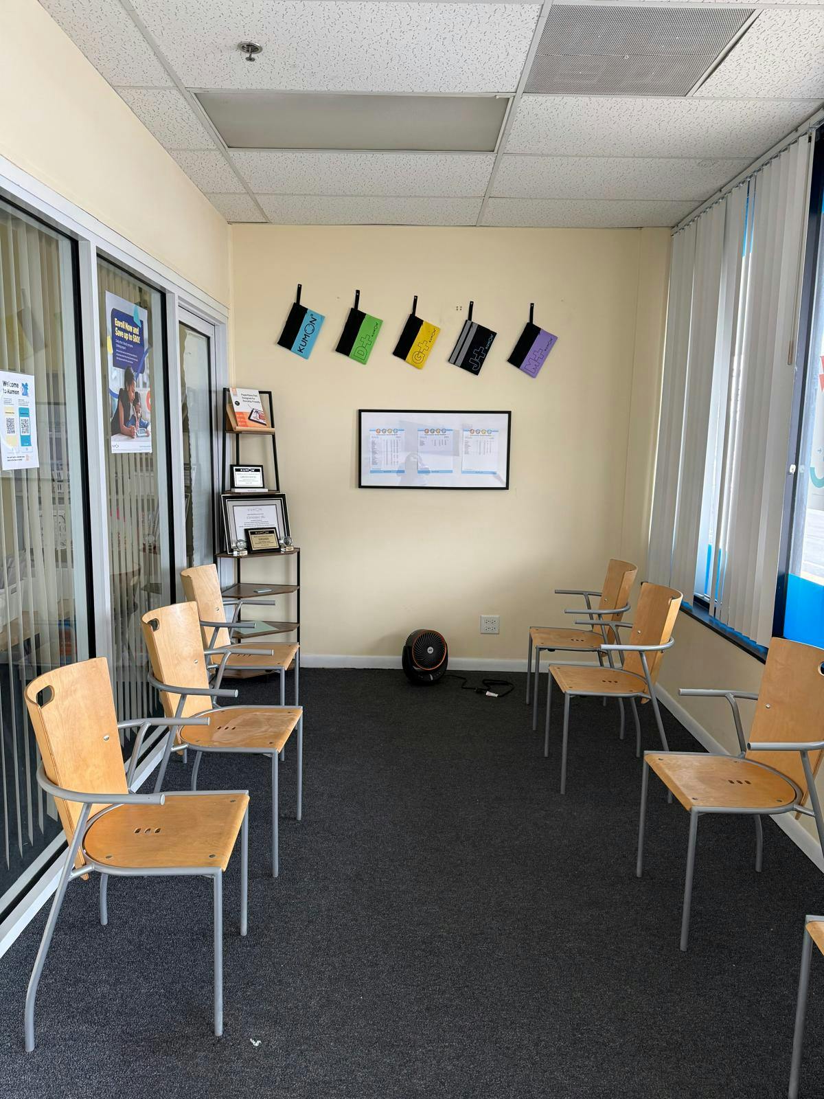 Empty waiting room with chairs, a small bookshelf, and a framed Kumon display