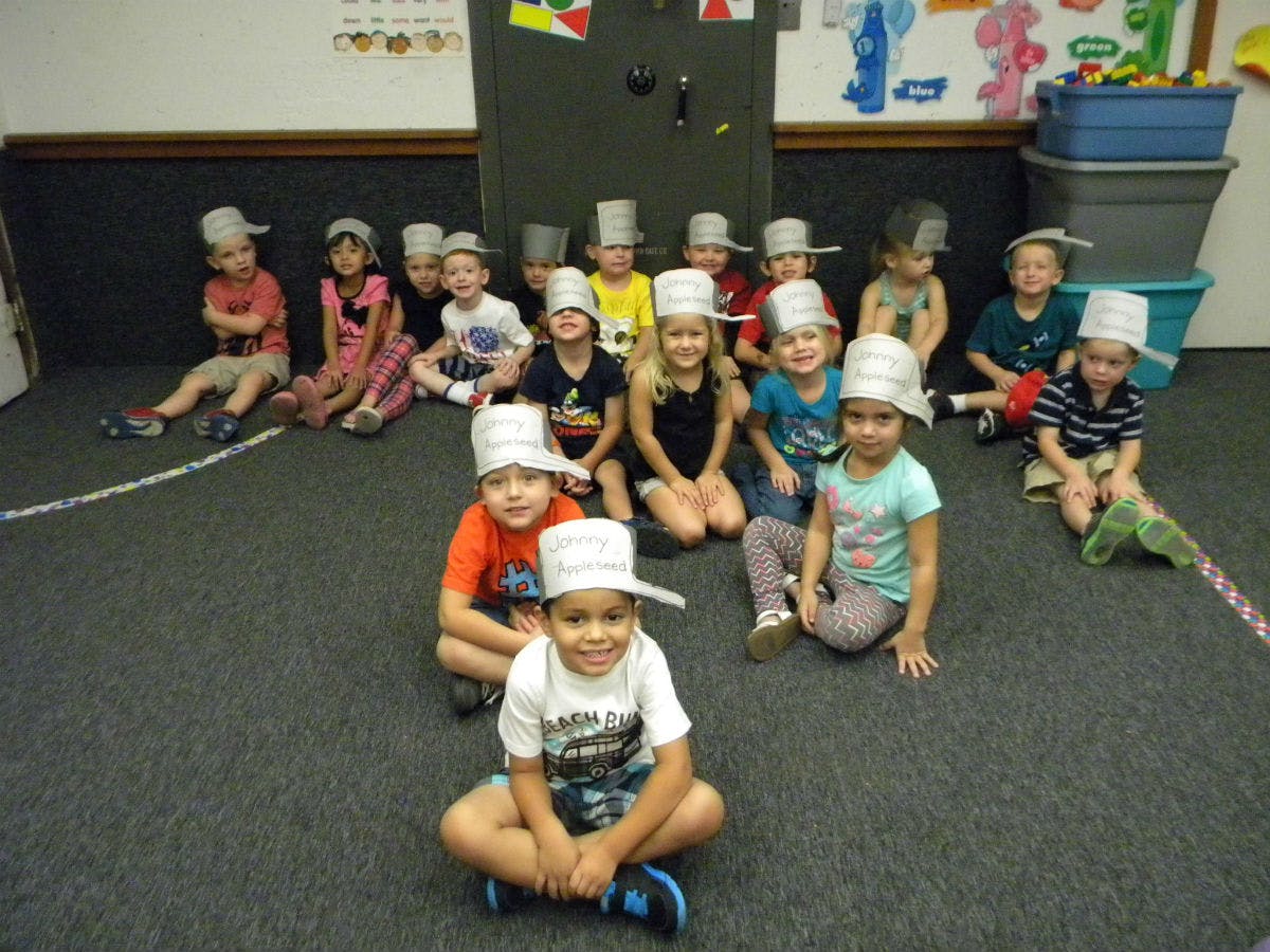 Group of children wearing paper hats sitting on a carpeted floor
