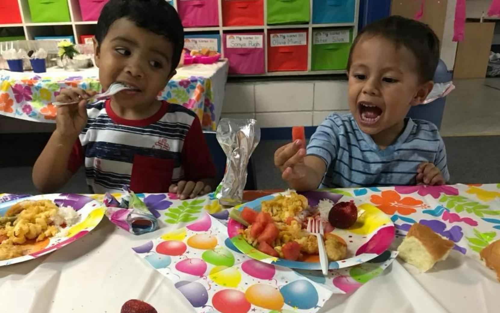 Two children eating at a table with colorful plates and patterned tablecloths