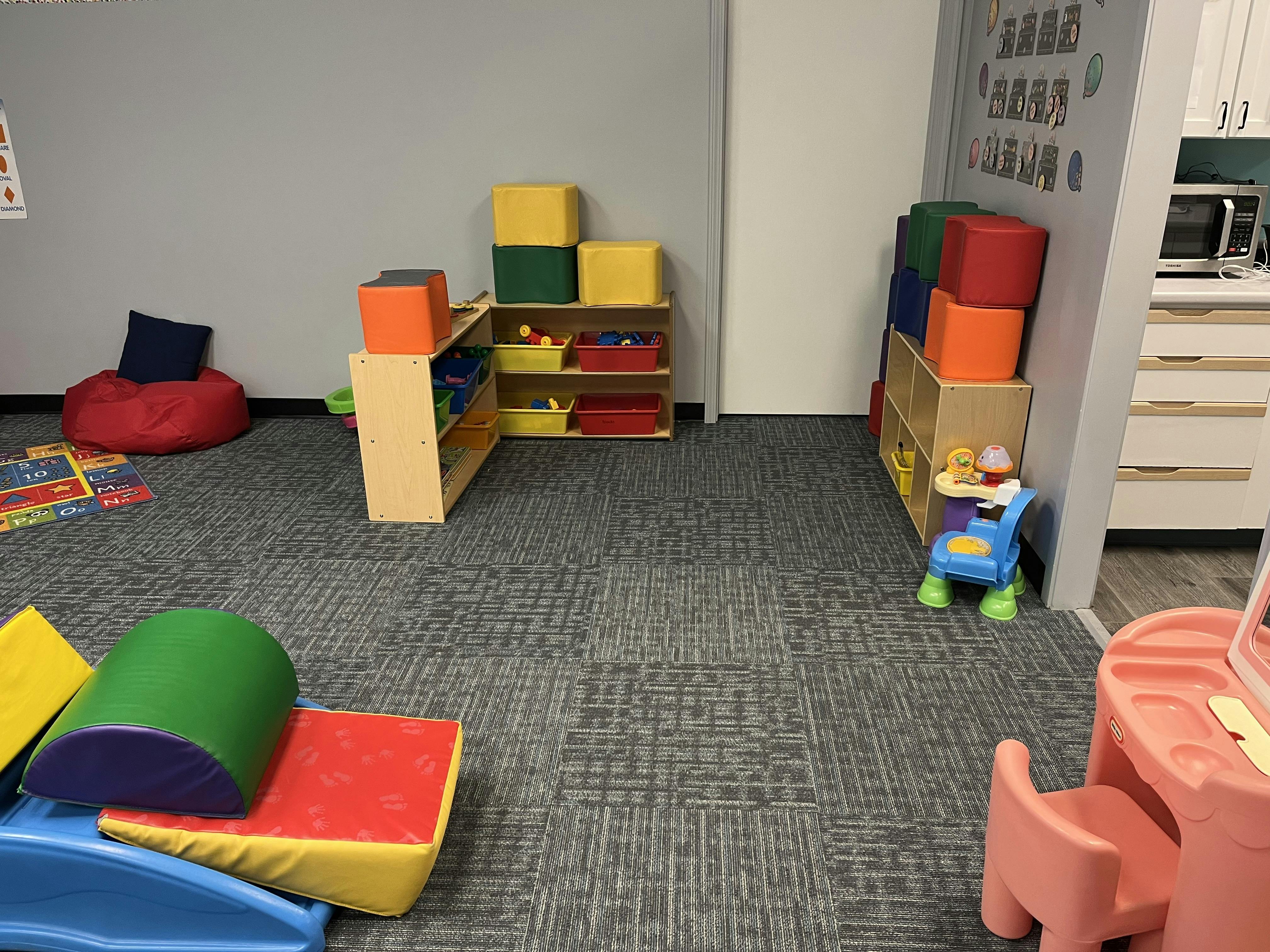 A playroom with colorful soft play equipment, toy shelves, and a red beanbag chair