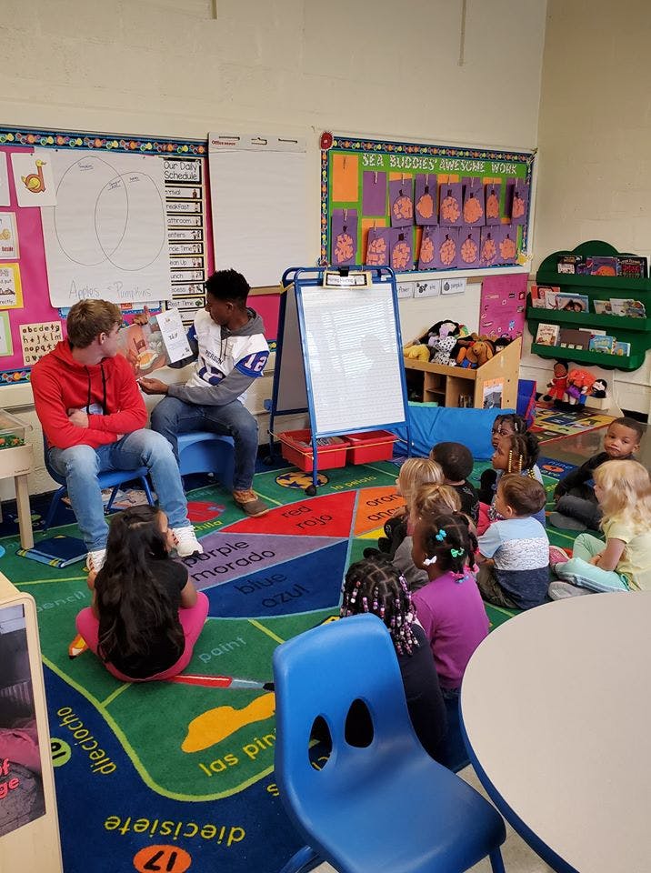 Two teens reading a book to a group of children in a classroom