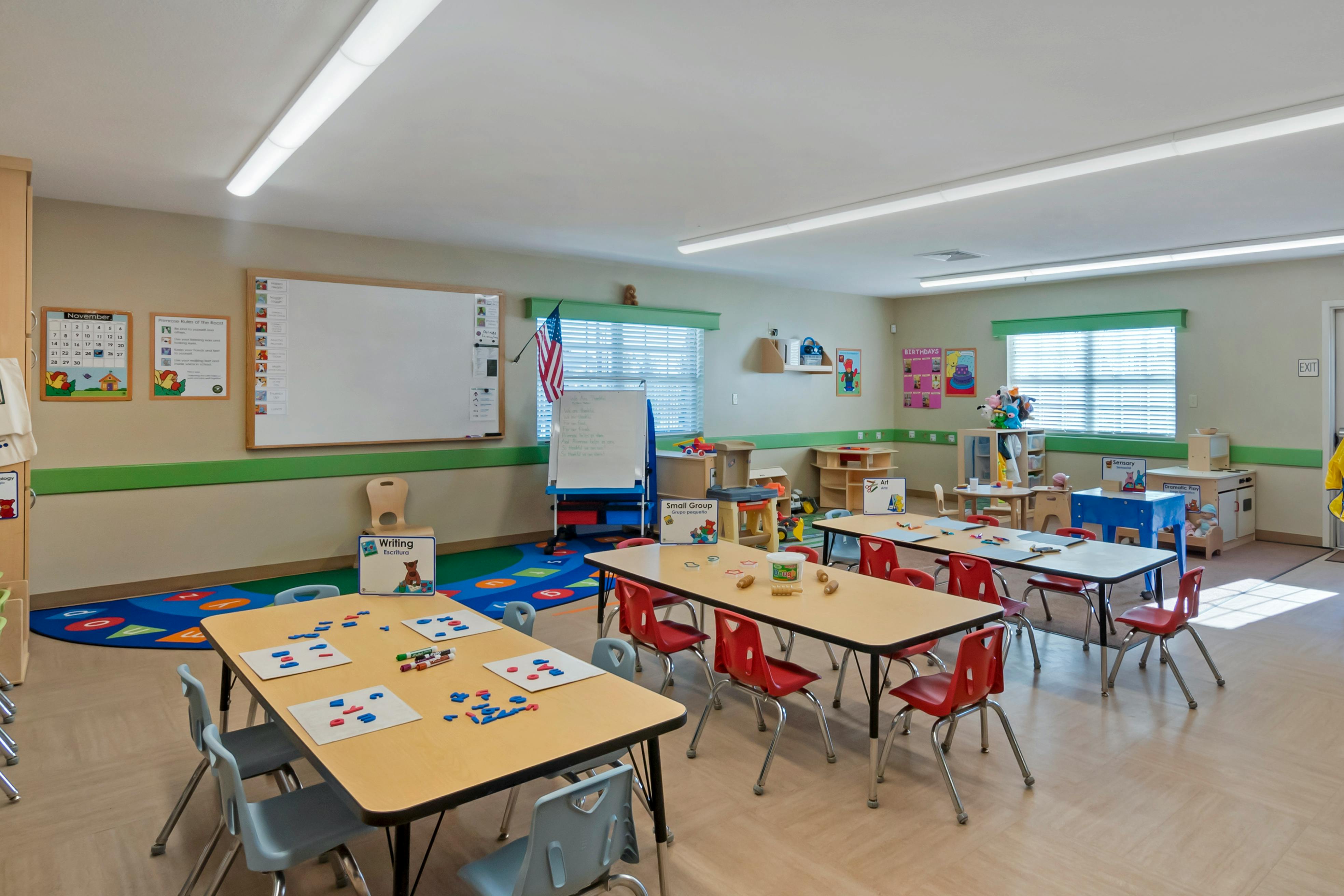 Classroom with child-sized tables and chairs, play area, and whiteboards