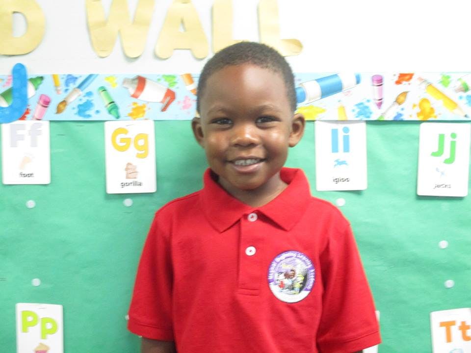 Child in red shirt standing in front of a green board with alphabet cards