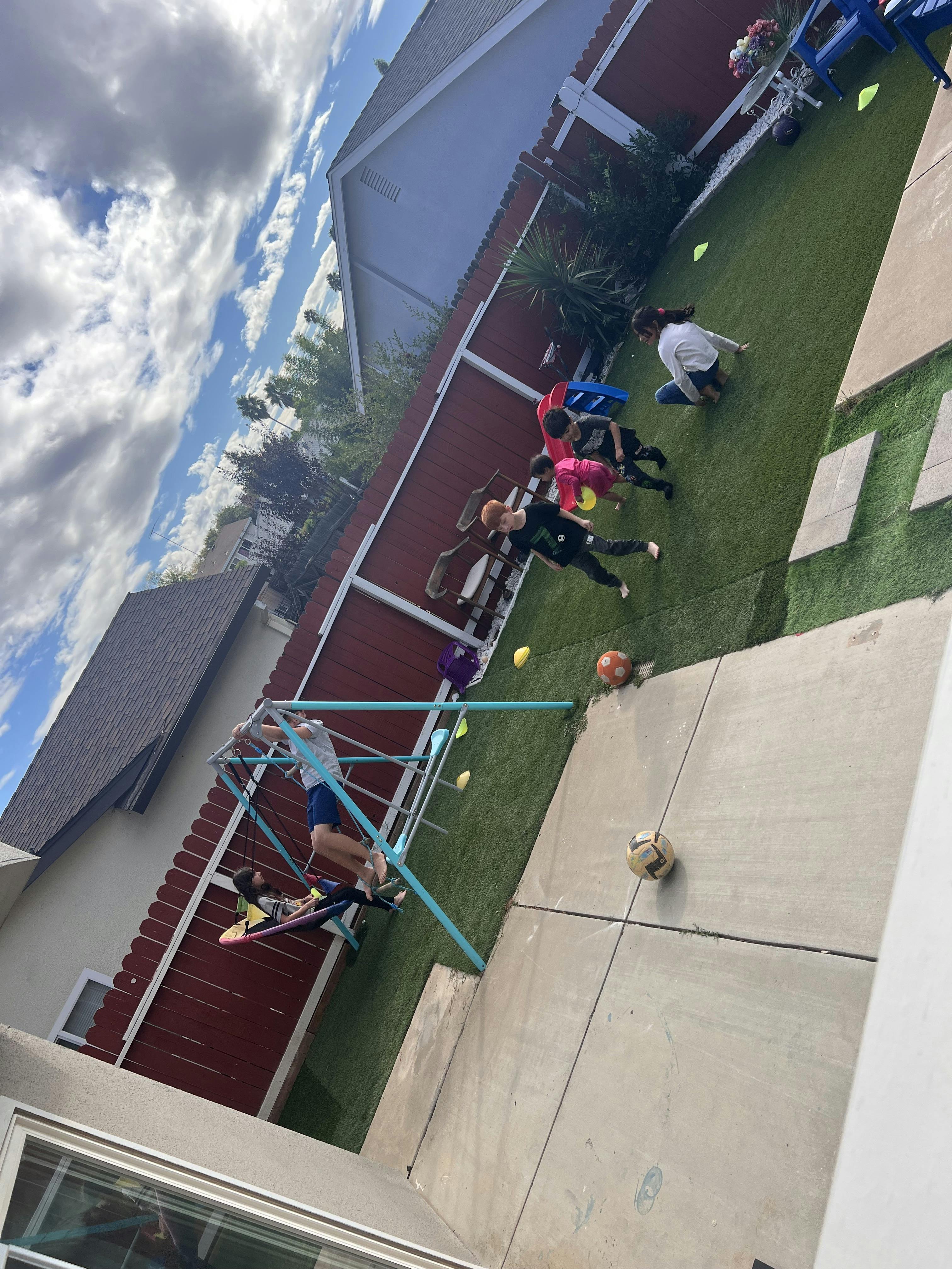 Children playing in a backyard with a swing set and soccer balls