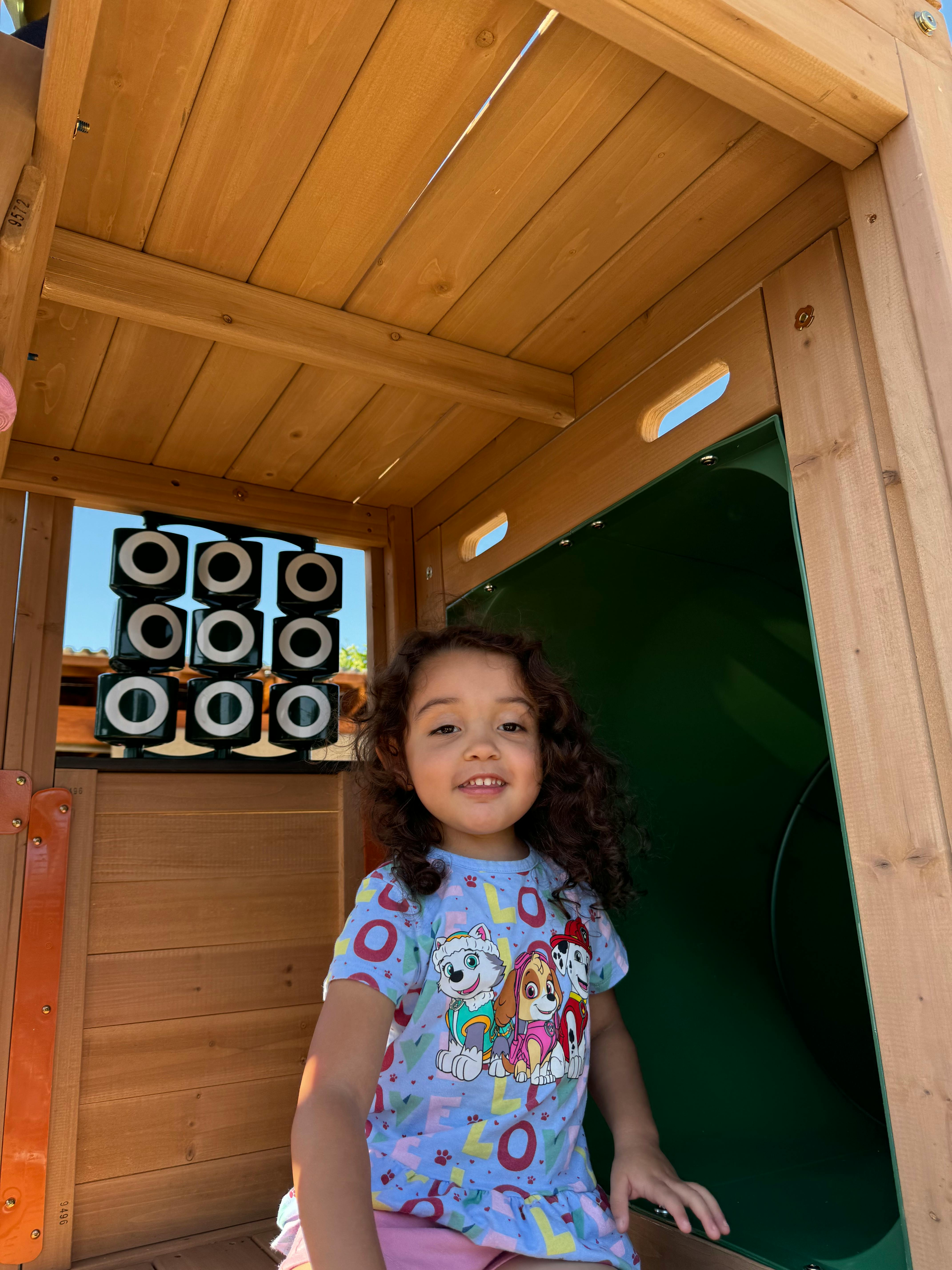Child in a wooden playhouse with a green slide