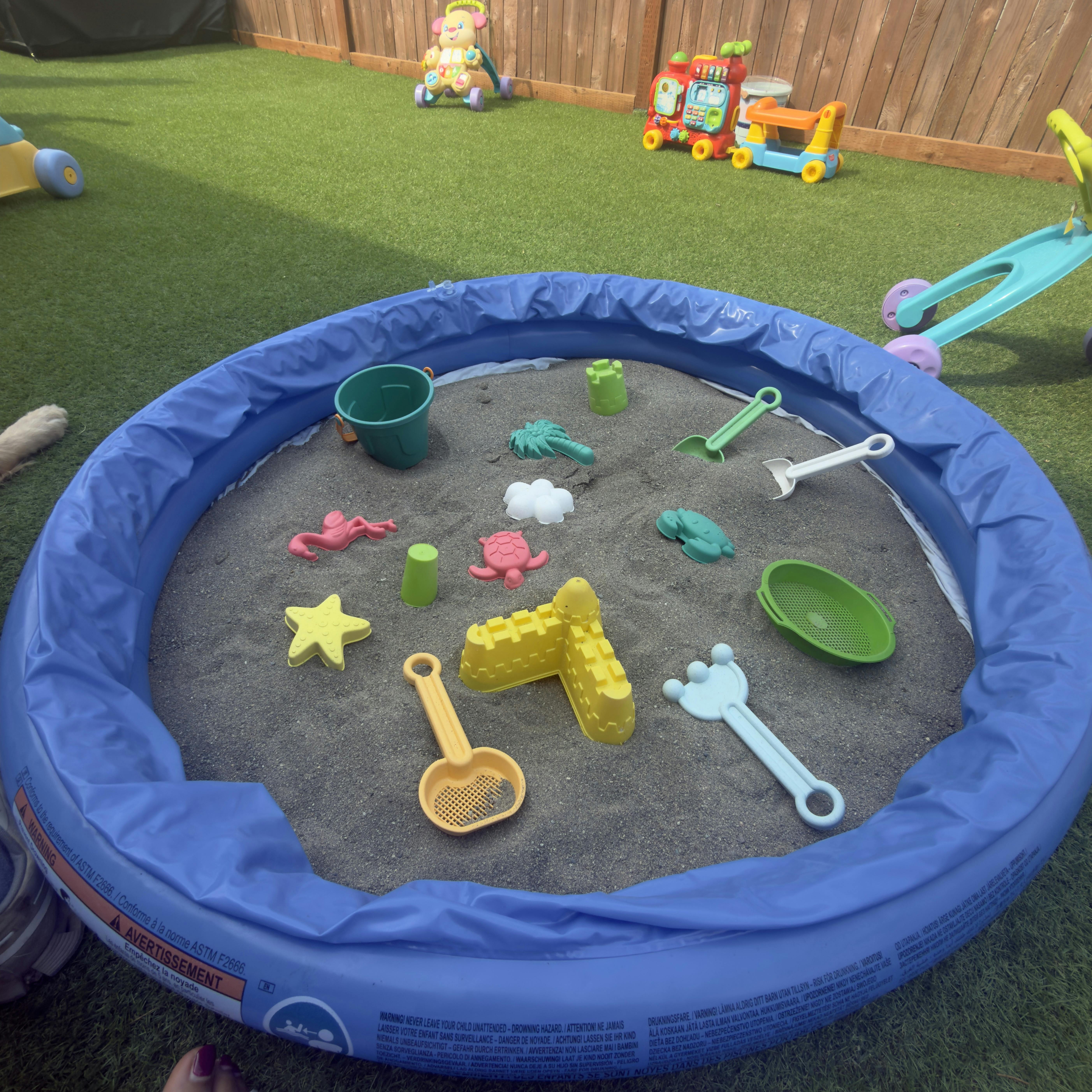 Plastic sandbox filled with sand and colorful toy molds on artificial grass