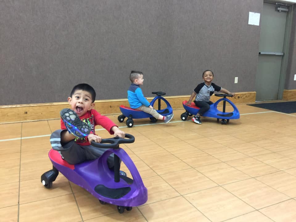 Three children riding on toy cars indoors