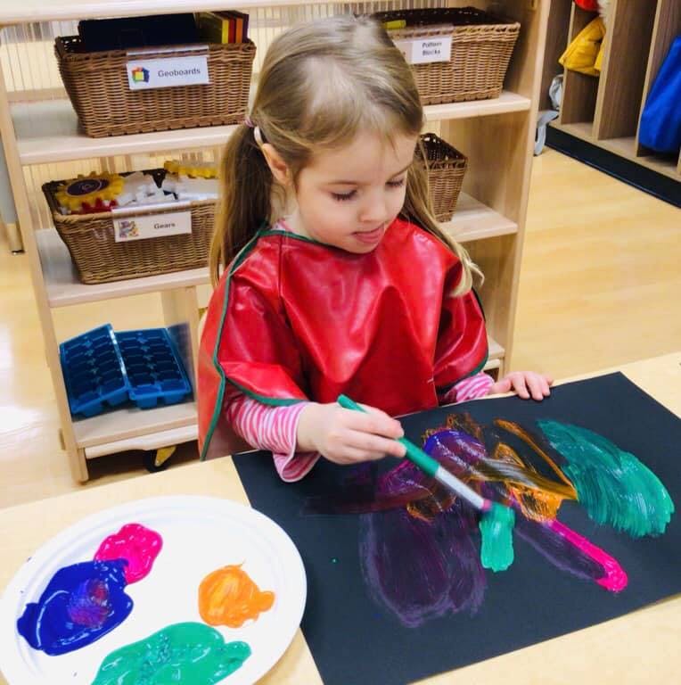 Child in a red smock painting on black paper with a paintbrush