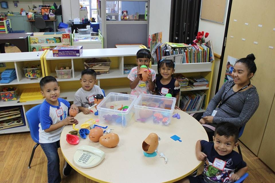 Adult and children playing with toys at a table in a classroom