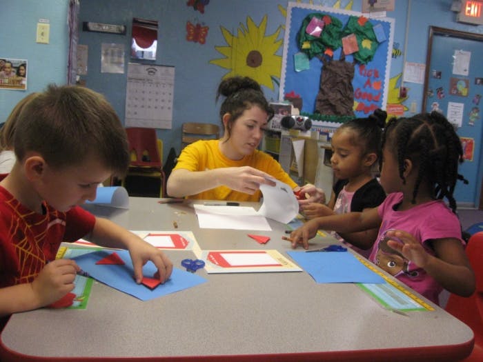 Adult and three children doing crafts at a table in a classroom