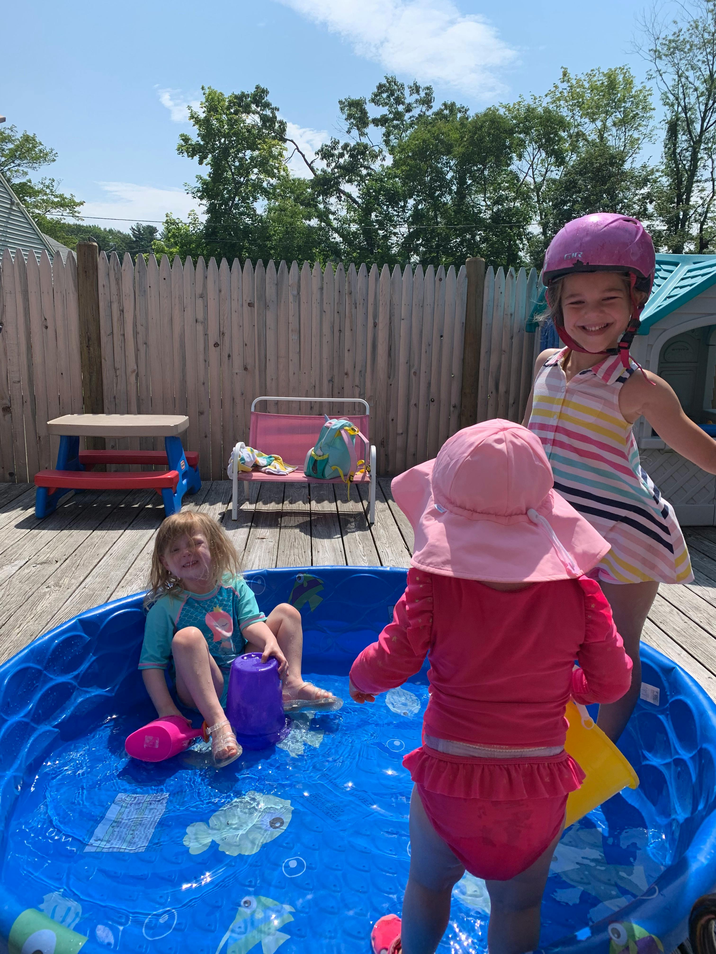 Three children playing in a blue wading pool on a wooden deck