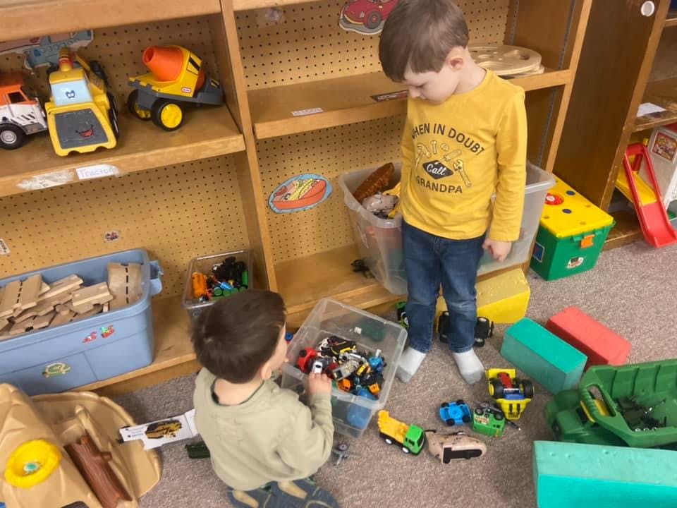 Two children playing with toy cars in a classroom