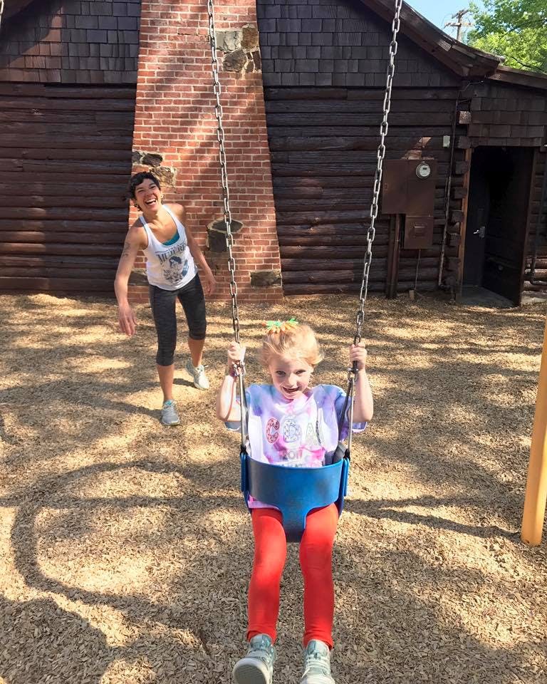 Child in a swing with a person standing behind